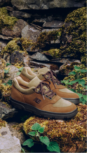 Un par de zapatillas New Balance Made in UK sobre una roca cubierta de musgo jard&iacute;n rodeado de peque&ntilde;as plantas verdes.