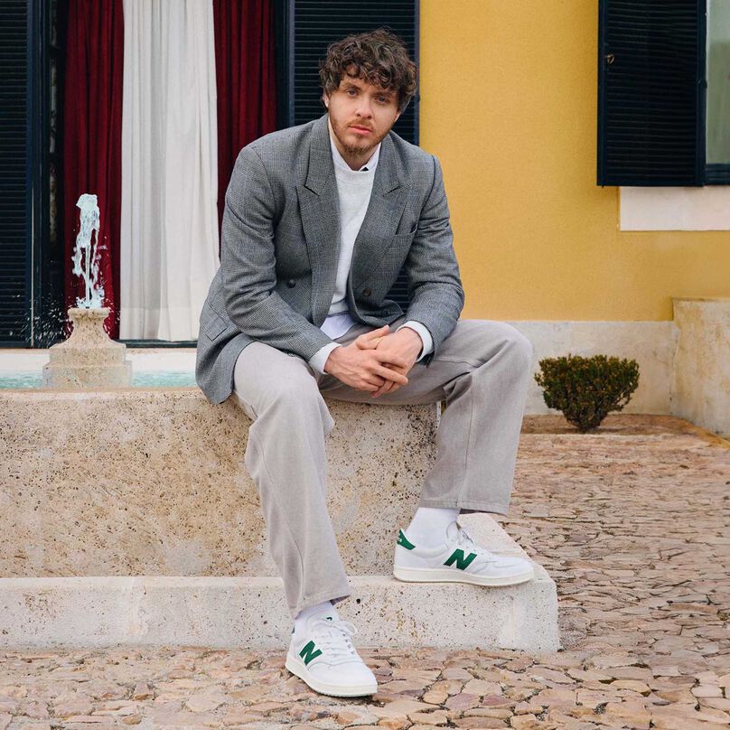 Jack Harlow sitting outside on a fountain.