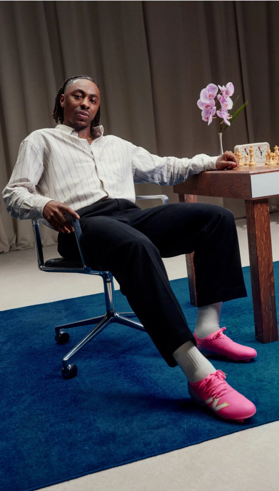 Eberechi Eze sentado en una silla junto a una mesa de ajedrez, con zapatillas New Balance de color rosa brillante.