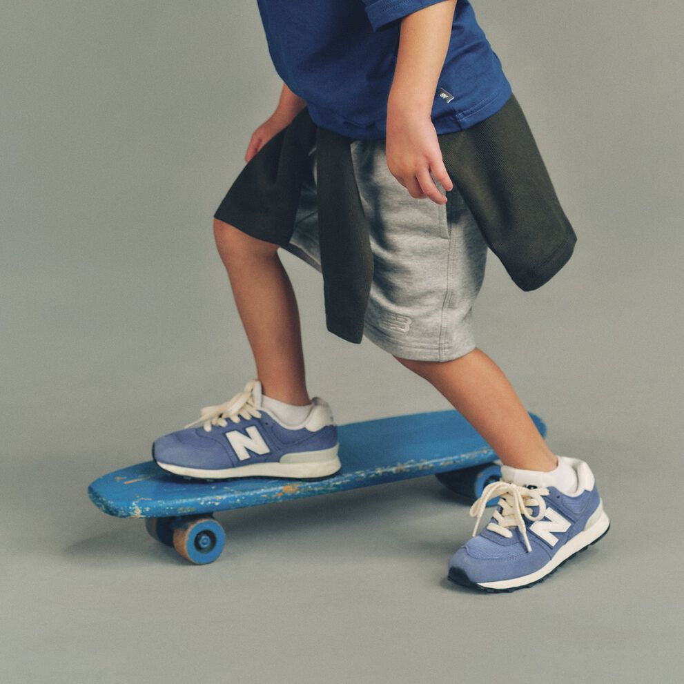 Studio image showing a child&rsquo;s lower body standing with one foot on a worn blue skateboard and the other foot on a smooth, light gray floor.