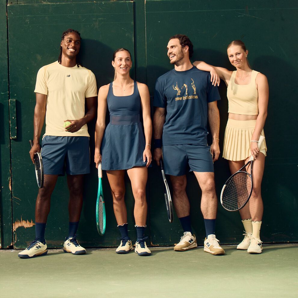 Four tennis players in coordinated athletic apparel stand against a dark green court wall holding rackets and a tennis ball.