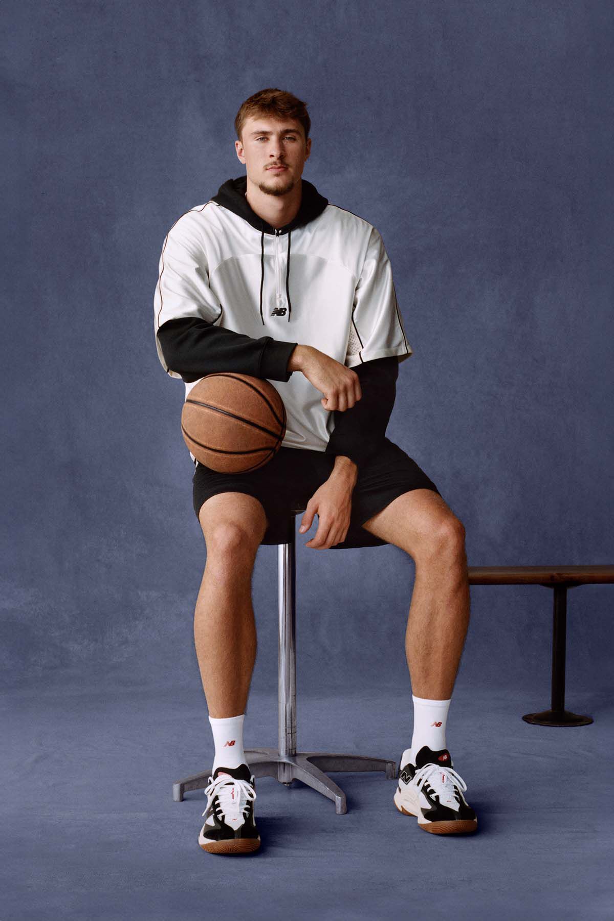 Cooper Flagg sitting on a bench and holding a basketball against a navy studio backdrop.