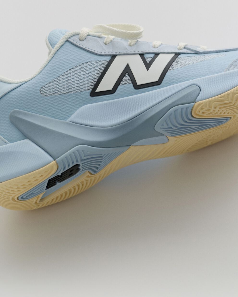 Close-up side view of a light blue New Balance basketball shoe featuring a mesh upper, large logo, and gum rubber outsole.