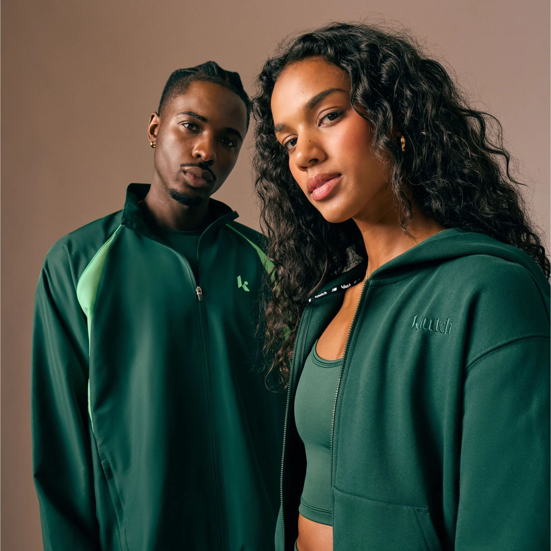 Young couple standing next to each other on a tan background in matching sets.