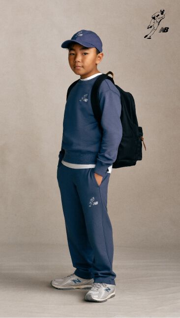 A little boy with wearing a blue set with a backpack standing with his hands in his pockets