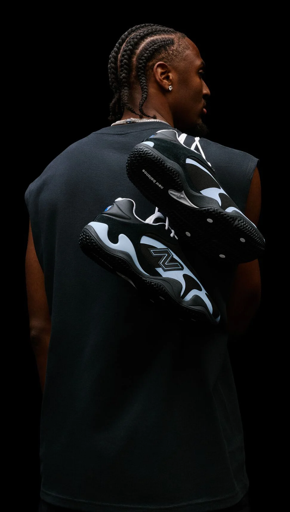 Studio portrait from behind featuring black-and-light-blue athletic sneakers suspended across a person's back against a black background.