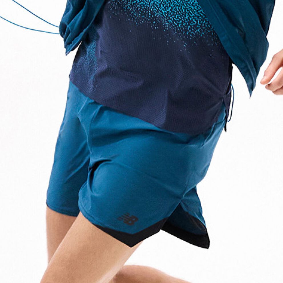 Primer plano de unos pantalones cortos de running color verde azulado en movimiento combinados con una camiseta de actuaci&oacute;n en capas sobre fondo blanco.