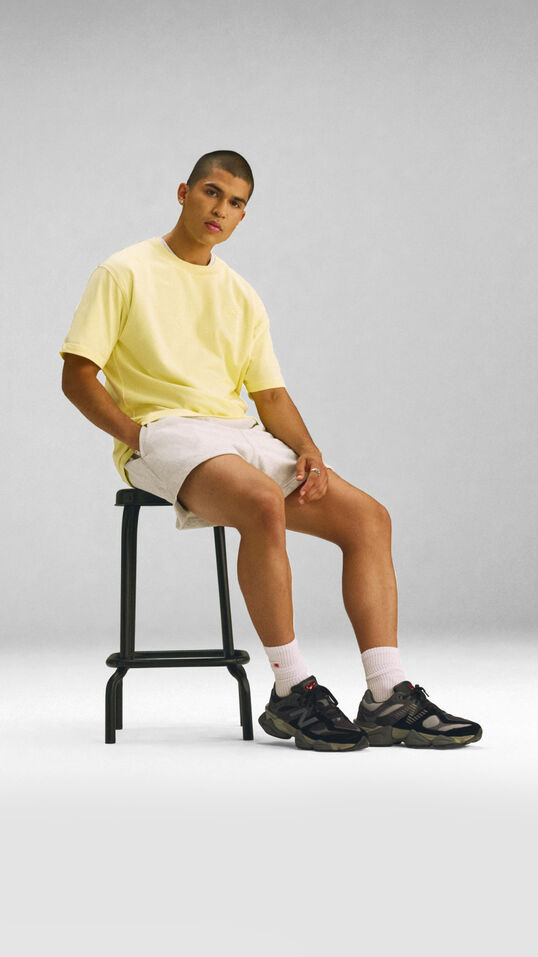 Young man sitting on a stool with a yellow shirt on a grey background. 