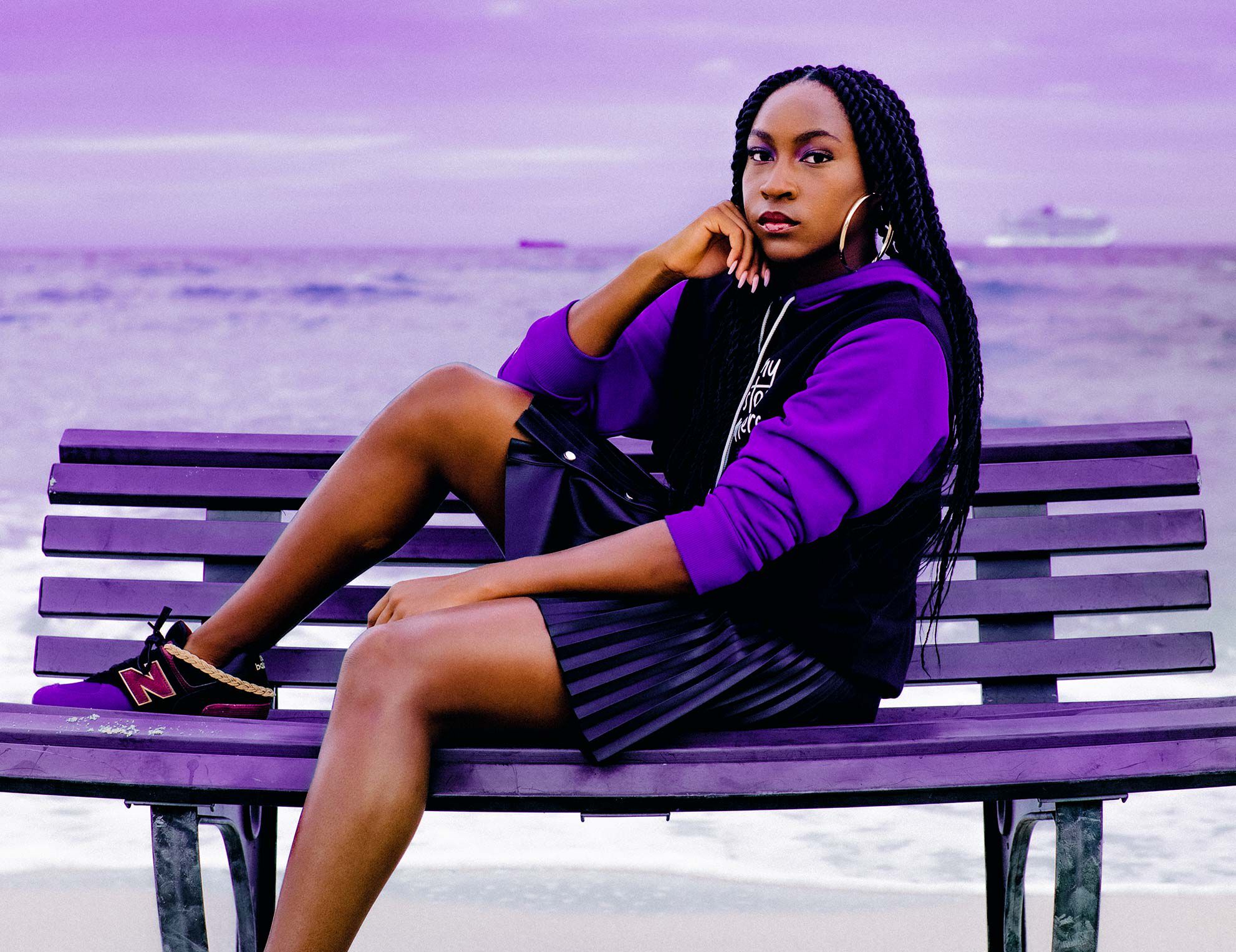 Coco Gauff sitting on a bench on the beach with the ocean in the background.