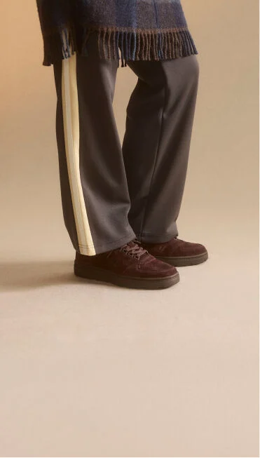 Waist down view of a woman wearing a pair of New Balance Made in UK sneakers standing in a beige studio environment.
