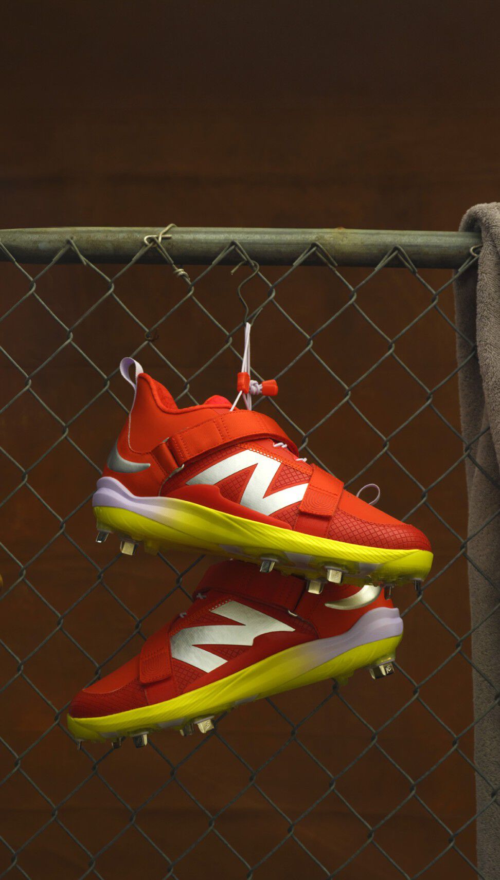 Pair of orange baseball cleats hanging from a chain-link fence in a dugout.    