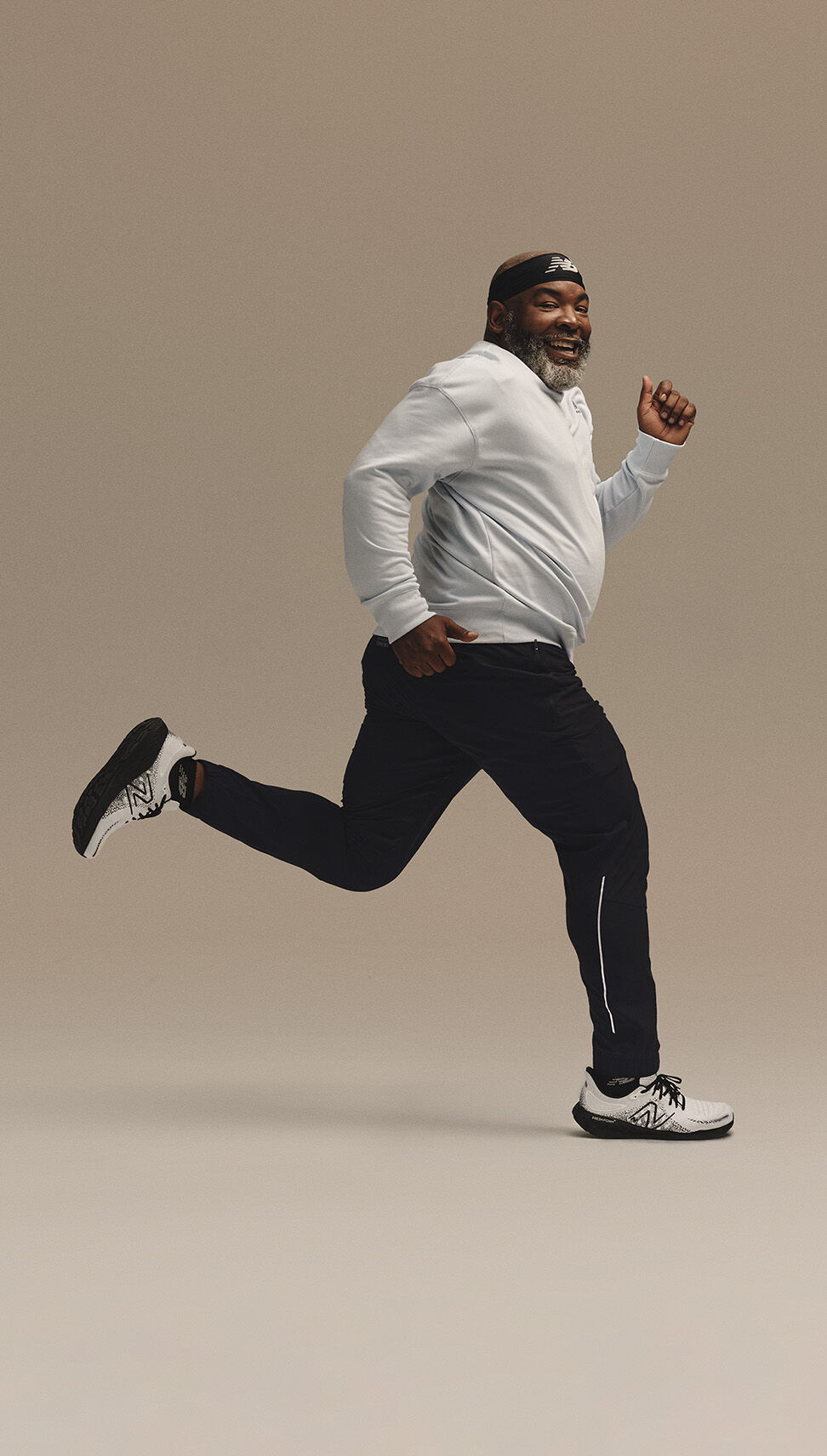Middle-aged man in a running pose in front of a beige studio backdrop wearing head-to-toe NB Running gear 