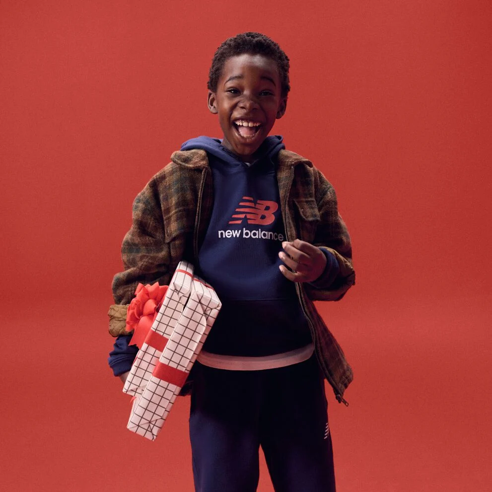 Niño riendo mientras sostiene regalos sobre un fondo rojo.