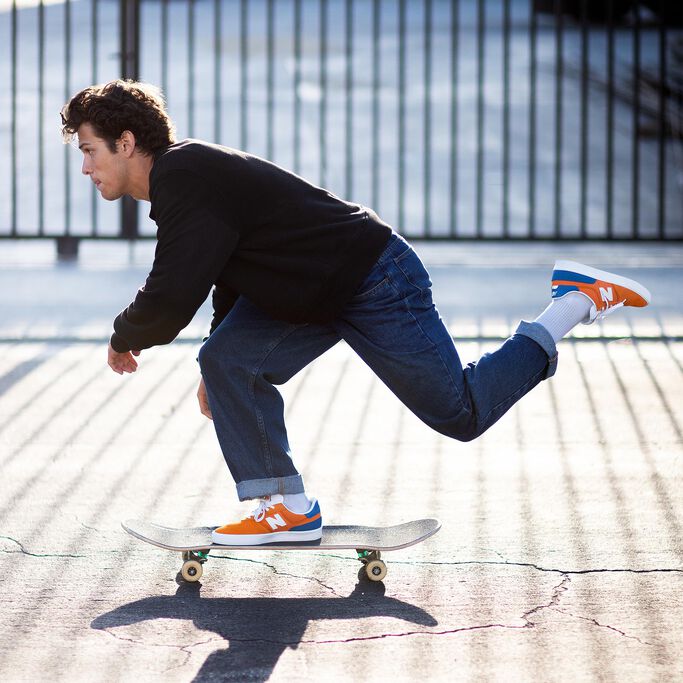 Profile view of pro skater Ronnie Kessner, mid-push on his skateboard, wearing orange NB Numeric 272 skate shoes