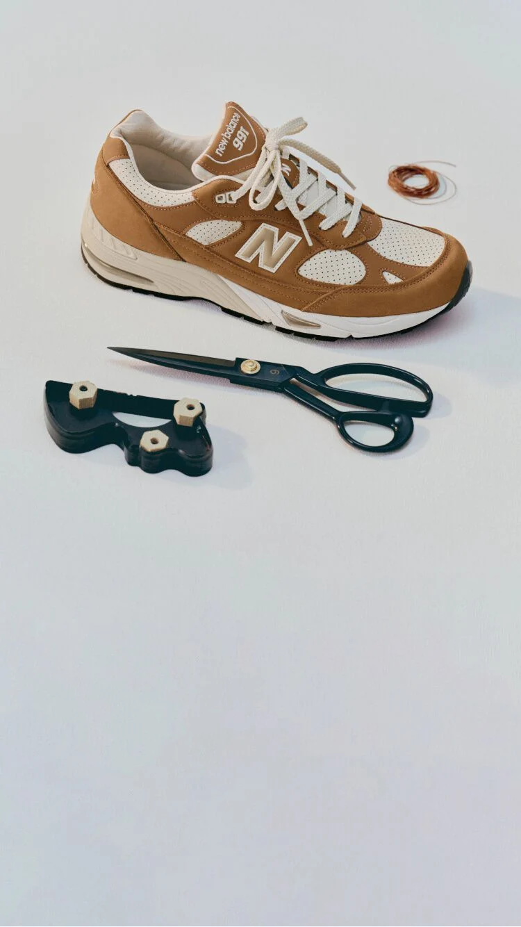 Zapatilla New Balance Made in UK en un entorno de estudio blanco rodeada de unas tijeras y herramientas de costura.&nbsp;
