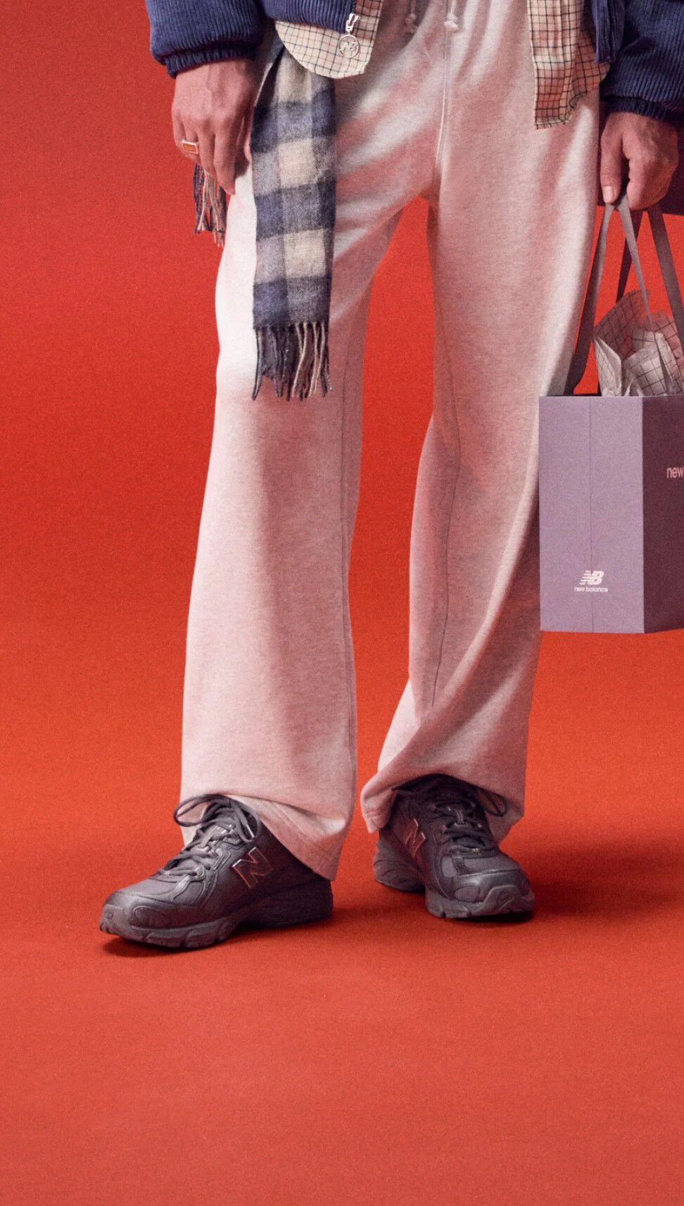 Young man standing on a red background holding a bag of gifts wearing grey sweatpants.