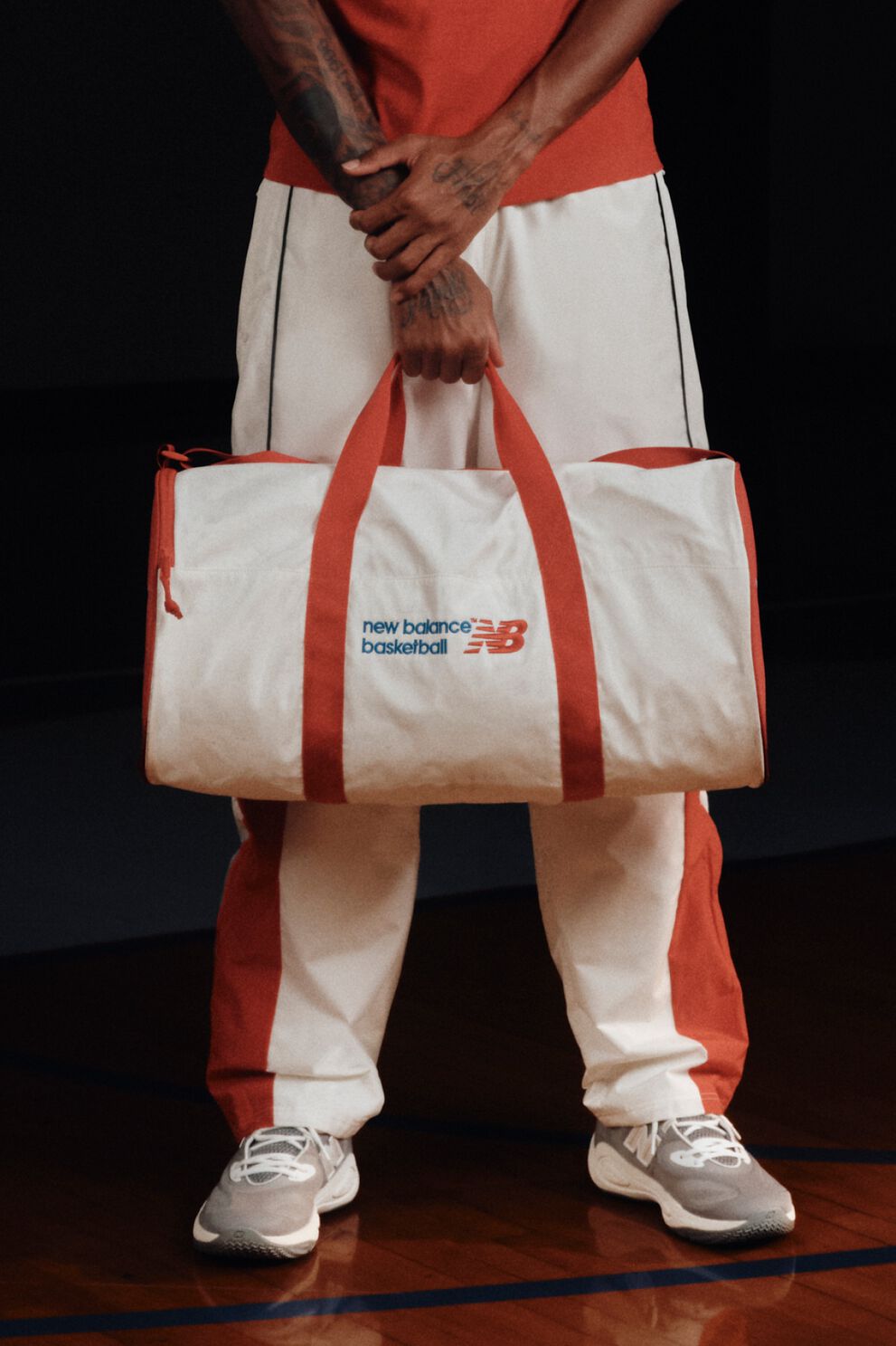 White and red New Balance Basketball duffel bag with red handles, held by a person in matching athletic apparel.