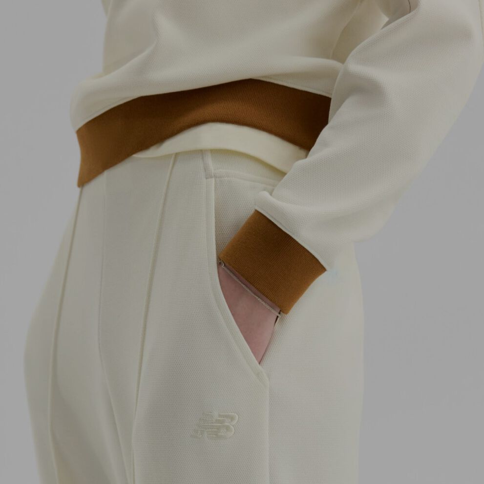 Close-up of someone wearing cream and brown New Balance pants on a white background. 