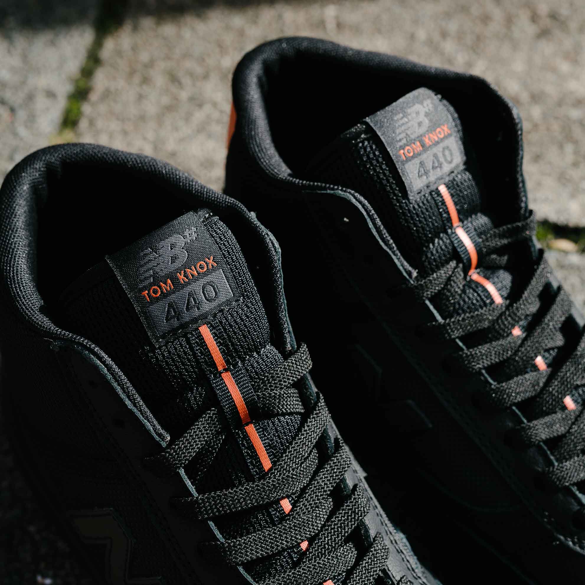 A pair of black hightop sneakers on pavement with dark shadows.