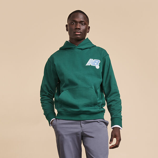 Man wearing green New Balance hoodie with grey pants posed against beige background in studio environment 