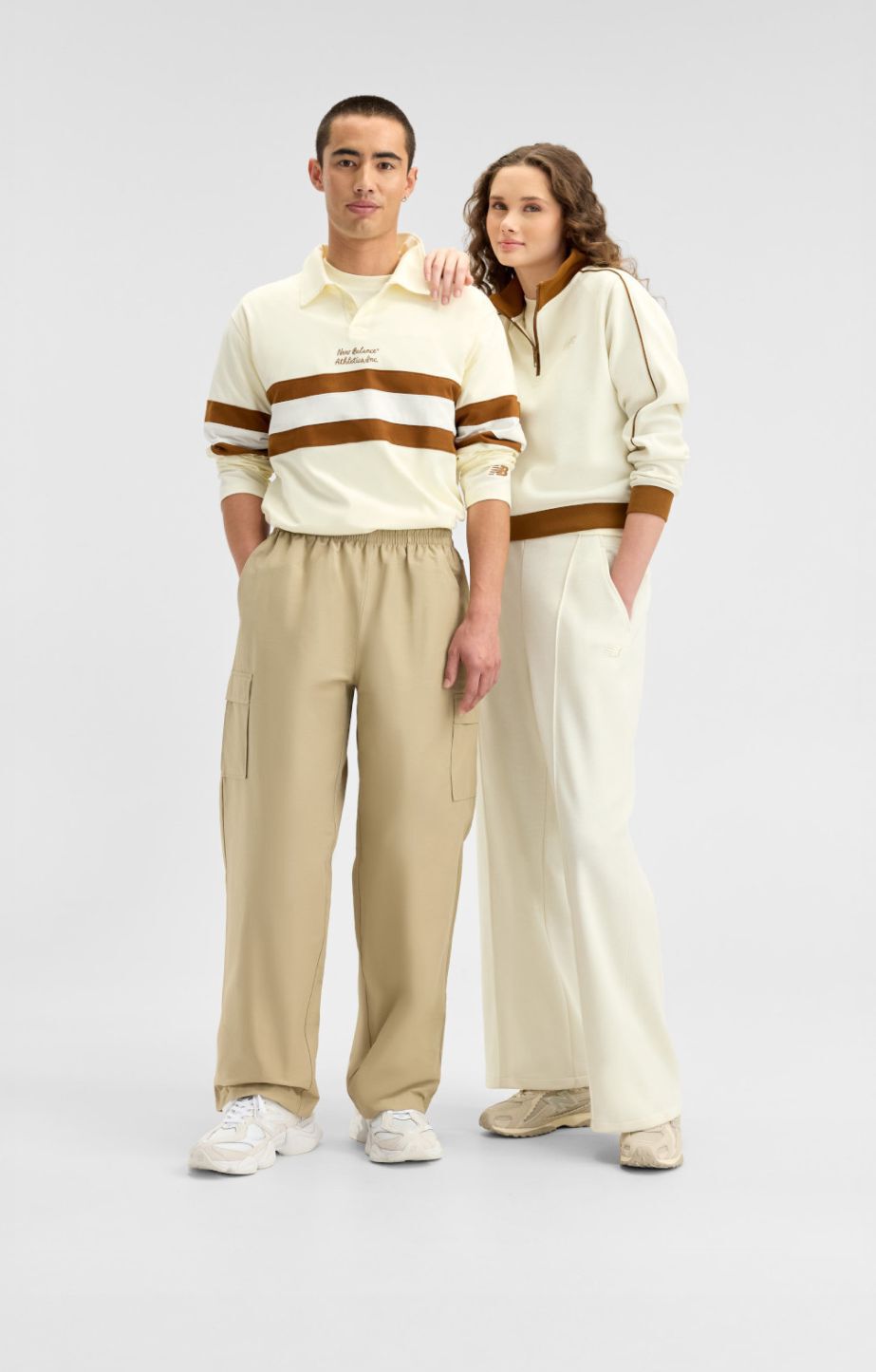  A man and woman wearing cream and brown New Balance gear on a white background. 