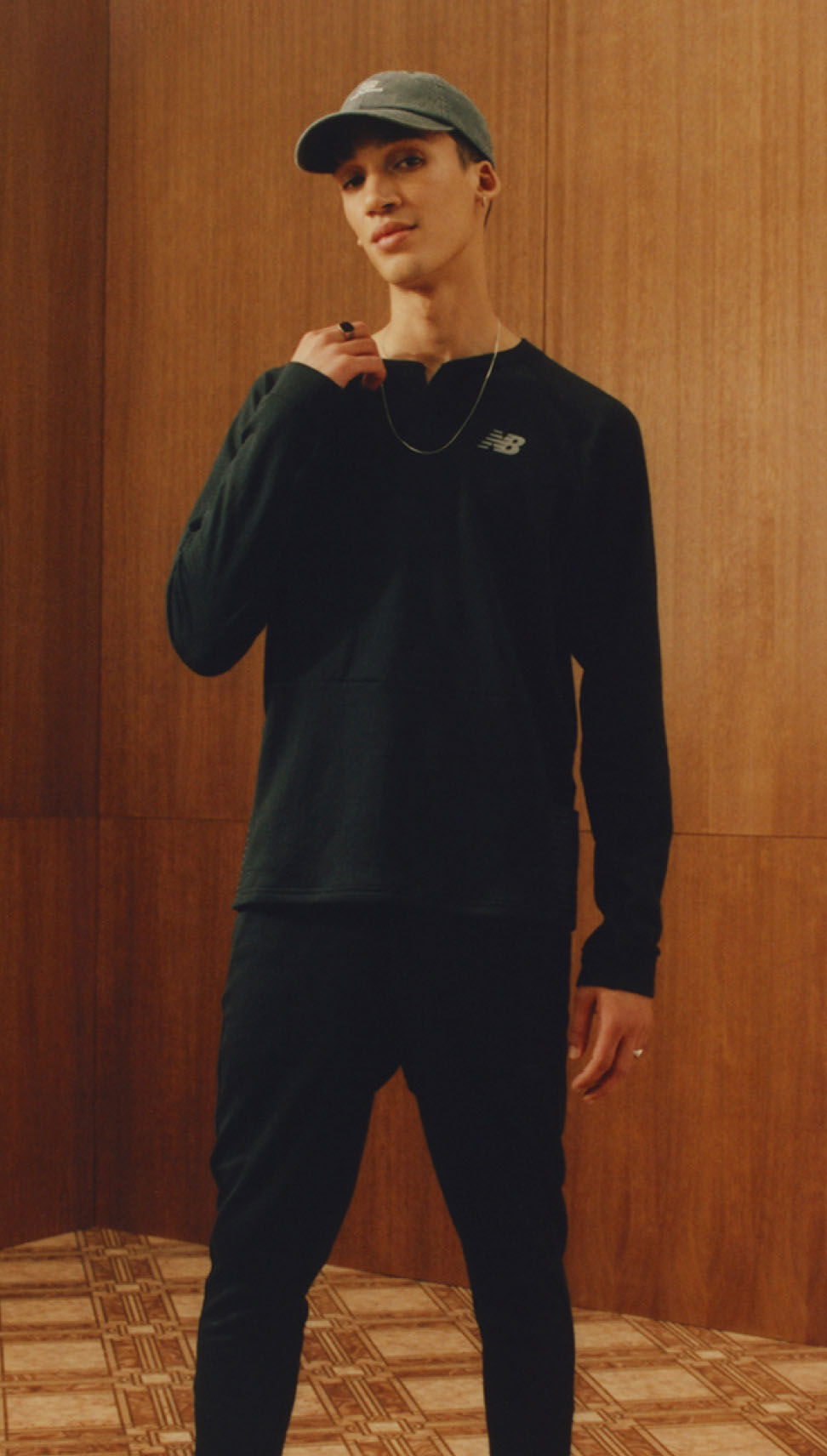 A man standing in an older wood vintage environment wearing all black New Balance apparel. 