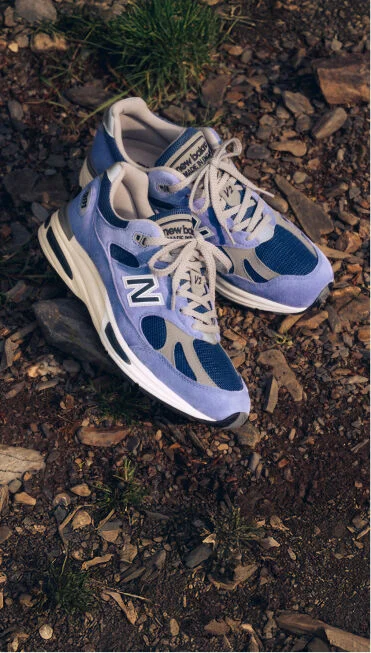 A pair of New Balance Made in UK sneakers on a raw earth surface of dirt and stones.