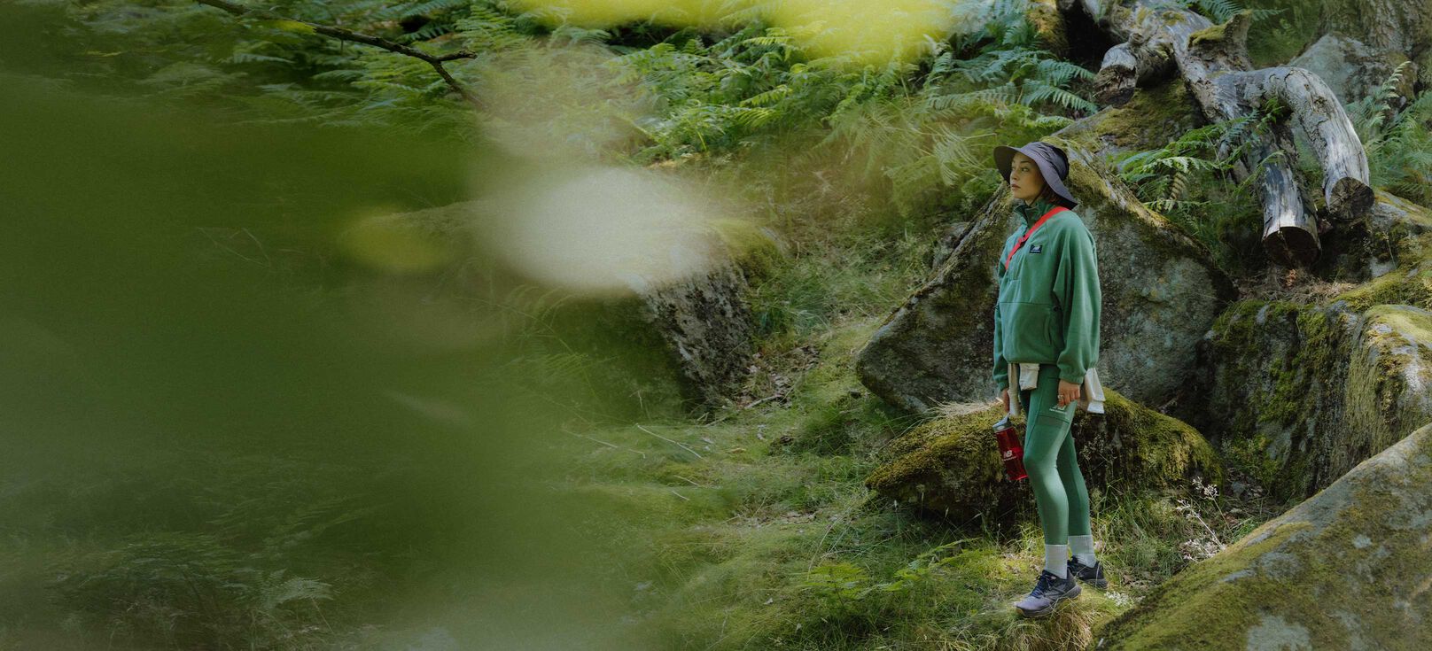 A person wearing New Balance apparel and trail shoes standing in a forest looking pensive.