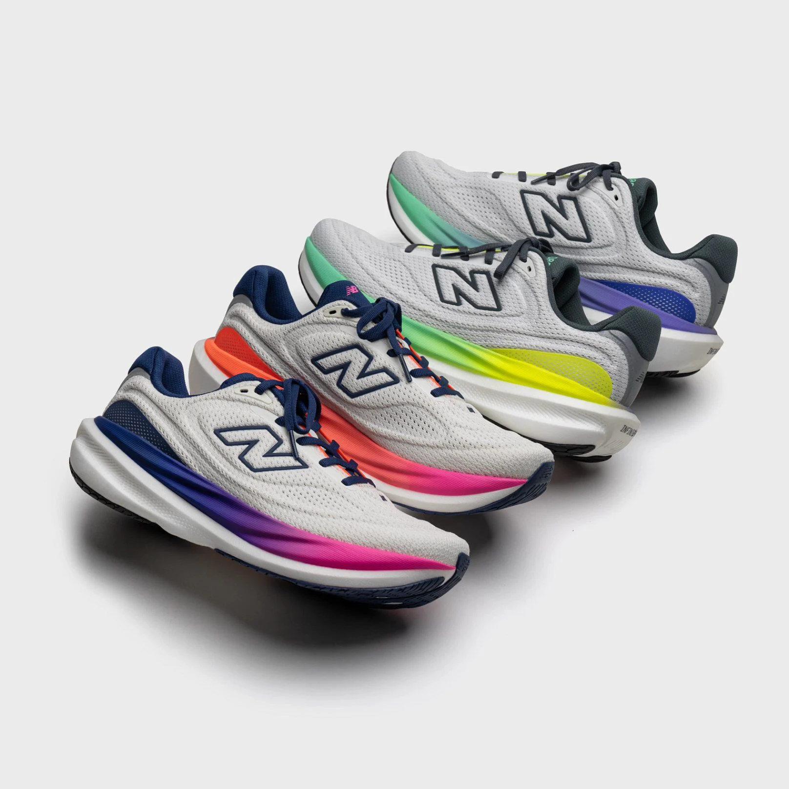 Four New Balance running shoes in light gray with white soles, each featuring a different gradient color detail: pink, orange, yellow, and green. 