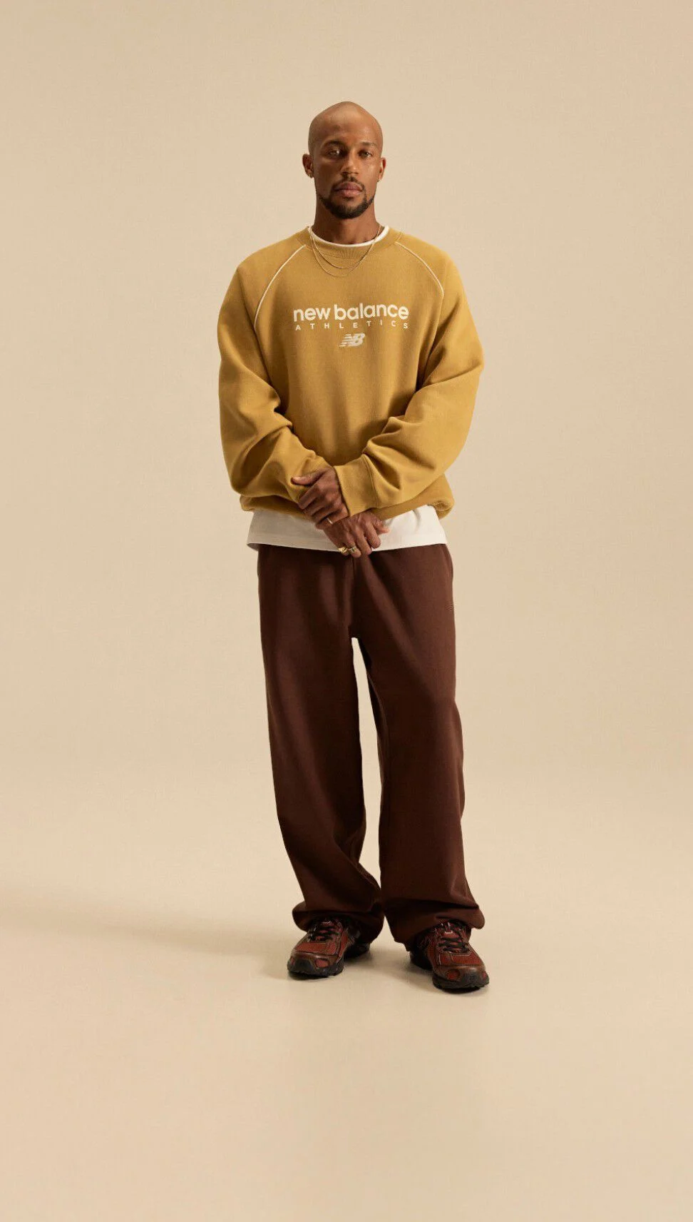 Image of Brian Reid in a New Balance outfit with a pale brown top in front of a beige background. 