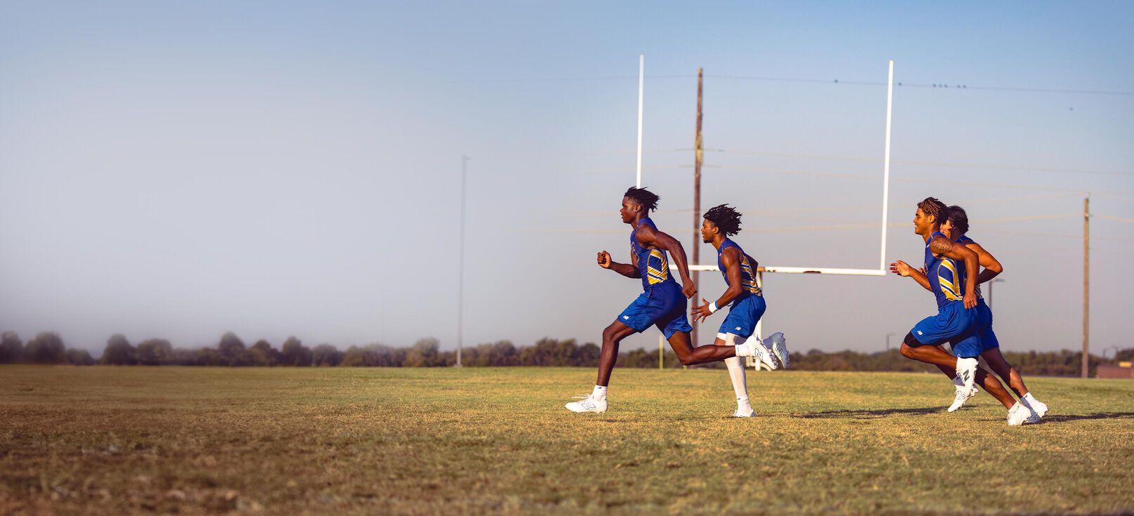 Atletas de fútbol americano de secundaria corriendo en un campo con tacos blancos de fútbol americano New Balance.