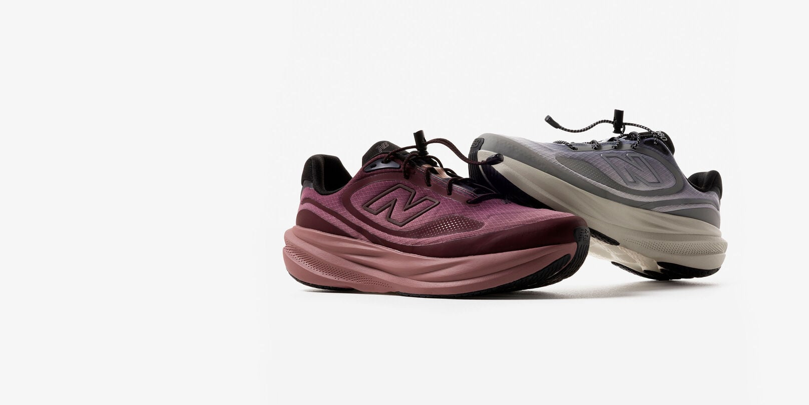 A plum colored and grey colored shoe stacked on each other against a grey studio backdrop