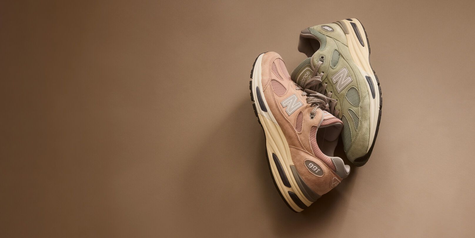 Top down view of two New Balance Made in UK sneakers resting against one another in a beige studio environment. 