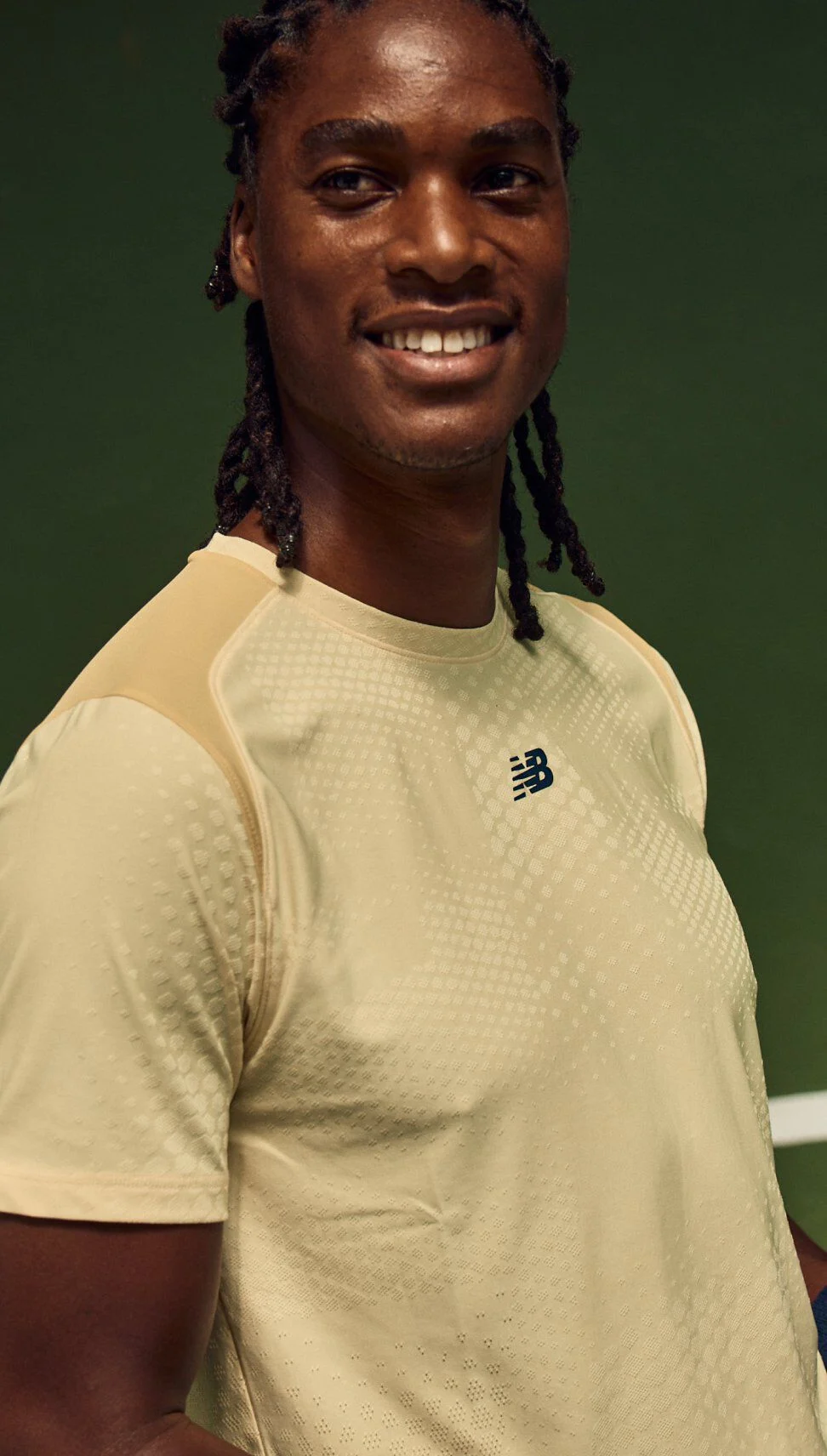 Close-up portrait of a tennis player wearing a light beige performance shirt with a textured pattern on an indoor court.