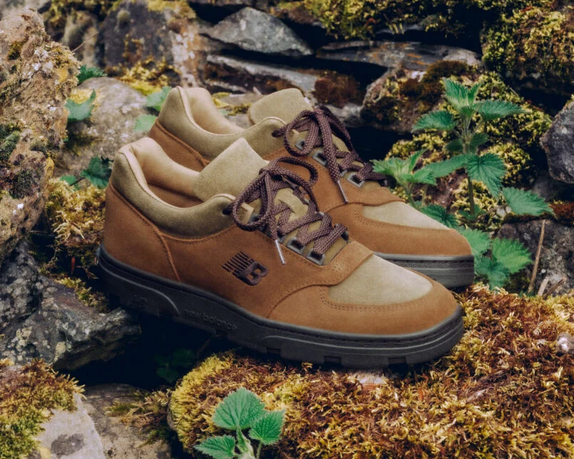 A pair of New Balance Made in UK sneakers sitting in a moss covered rock garden surrounded by small green plants.