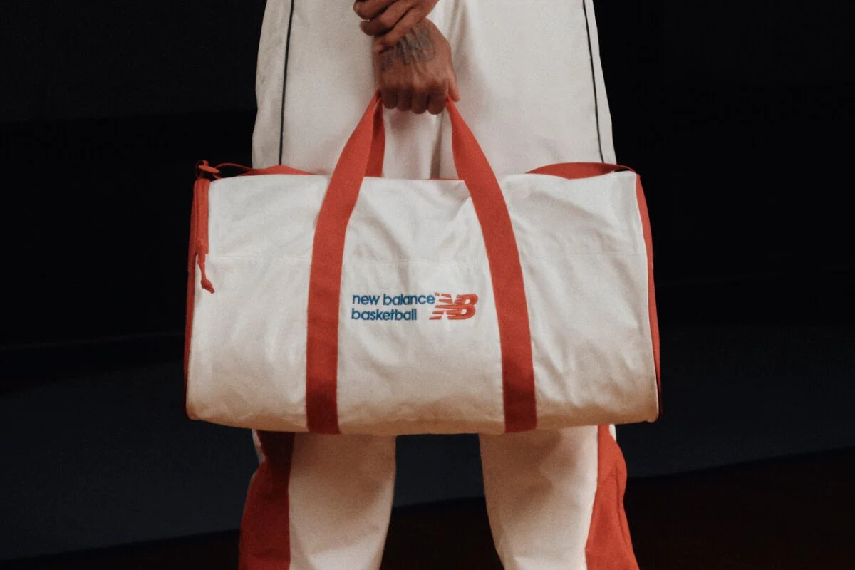 White and red New Balance Basketball duffel bag with red handles, held by a person in matching athletic apparel.