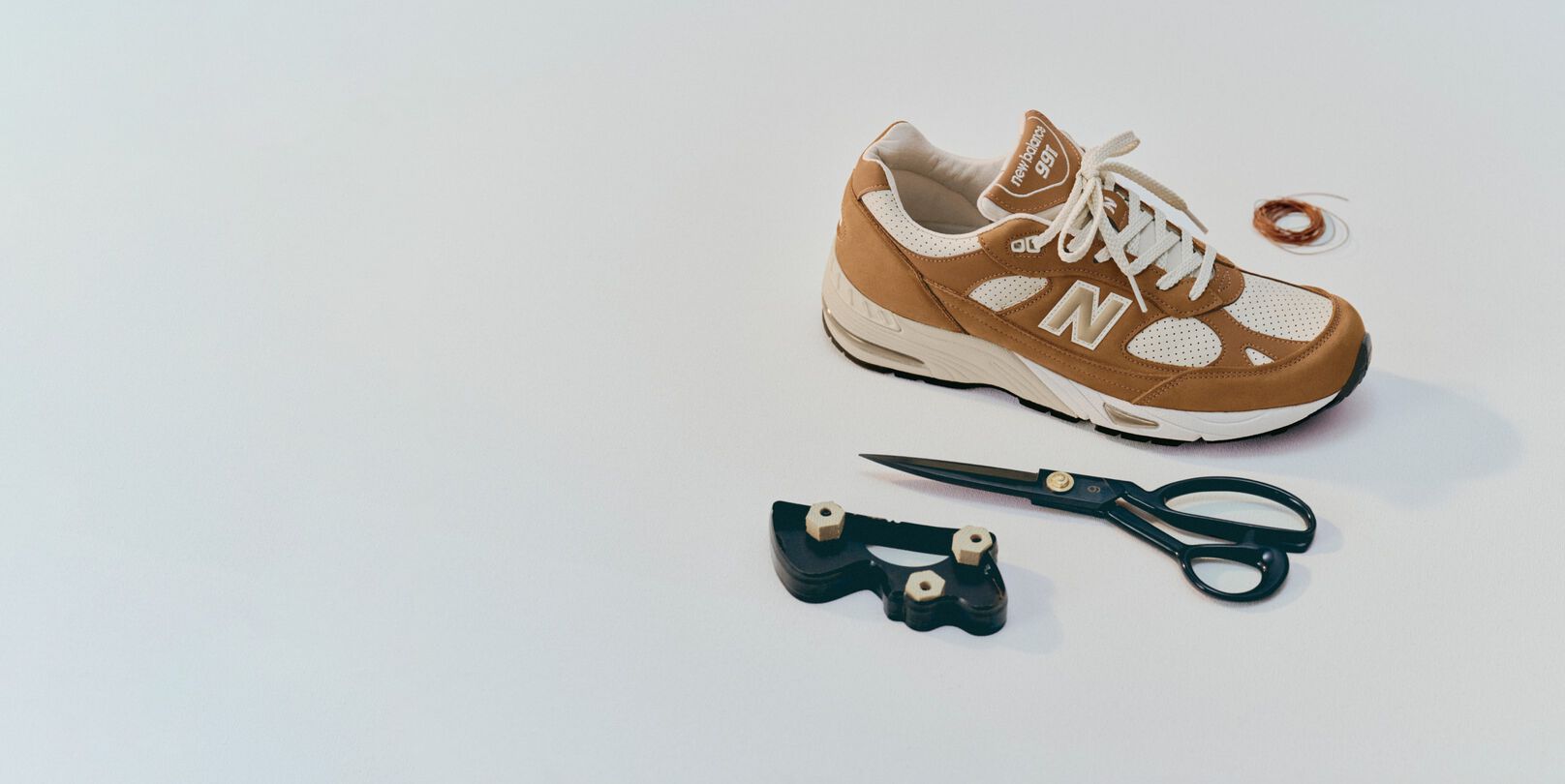Zapatilla New Balance Made in UK en un entorno de estudio blanco rodeada de unas tijeras y herramientas de costura.&nbsp;