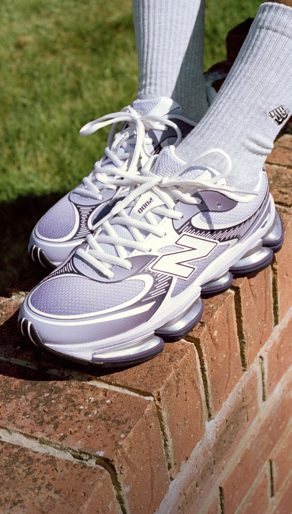 Close-up of someone wearing New Balance sneakers on a brick background.