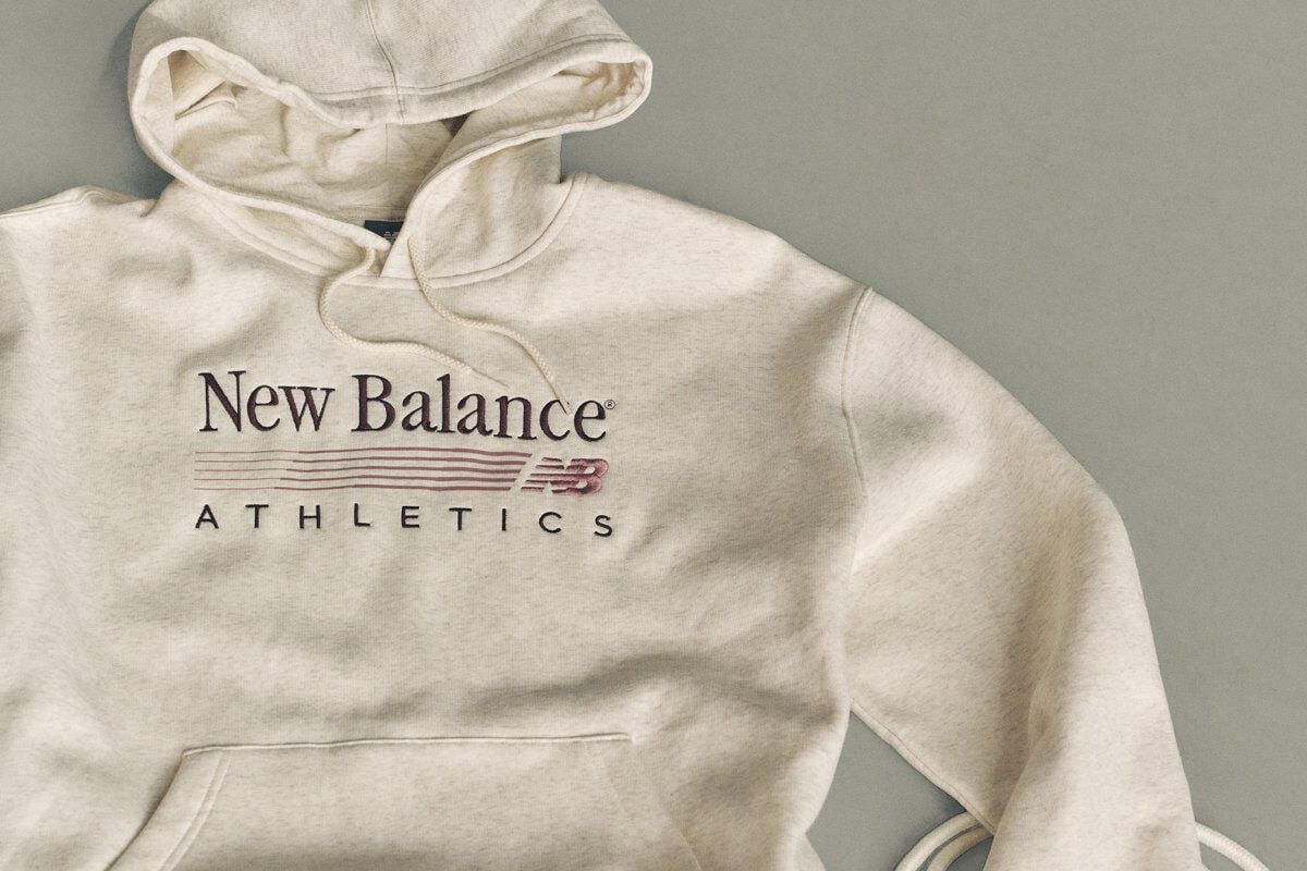 Flat lay studio image of a light beige hooded sweatshirt placed on a smooth, light gray background.