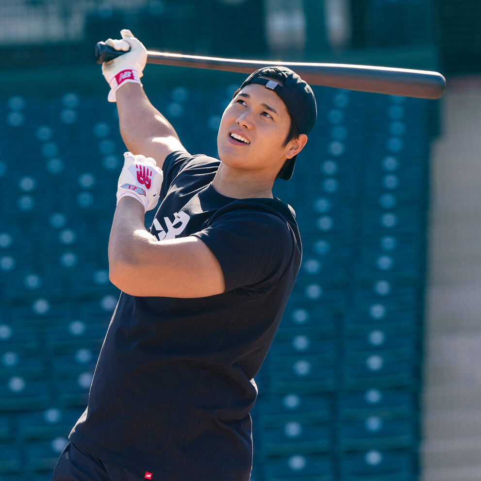 Young man in a black t-shirt swinging a bat in a stadium.  