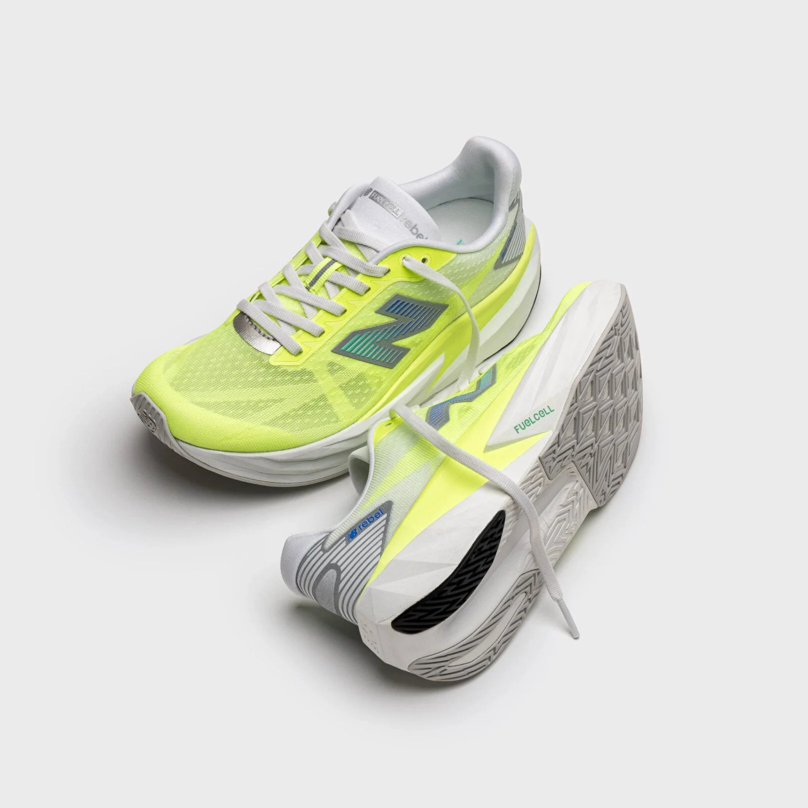 Pair of lime‑yellow running shoes with white midsoles and blue New Balance logos, displayed on a light gray background with one shoe upright and the other tilted to show the outsole. 