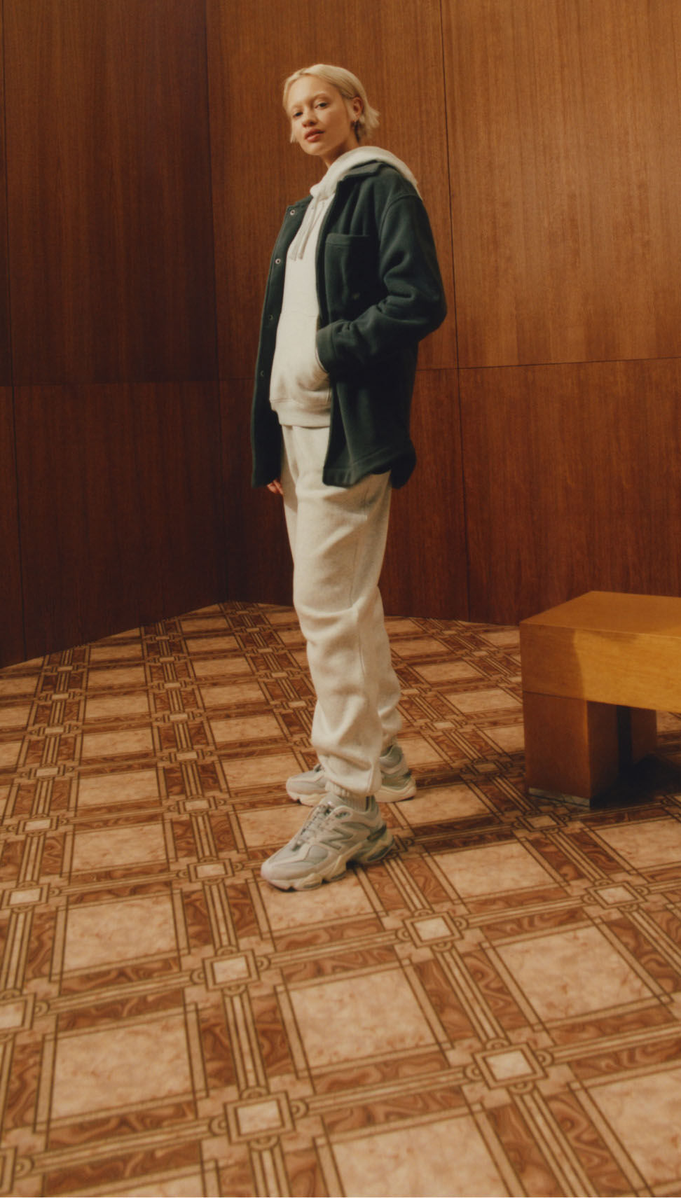 Una persona de pie en un entorno de madera y azulejos vintage con ropa y calzado New Balance. 