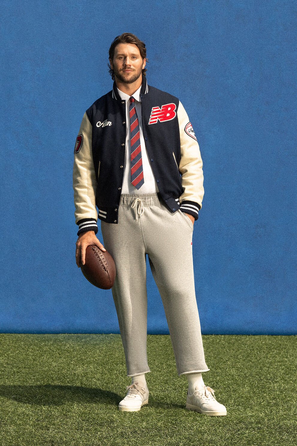 Josh Allen standing in front of a blue wall on green turf holding a football.