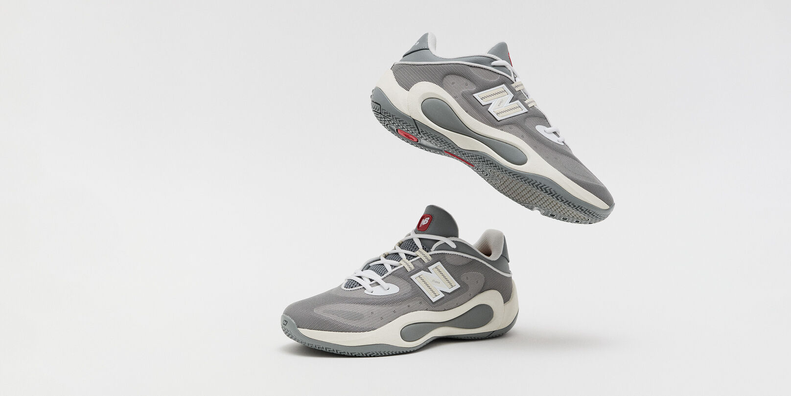 Gray New Balance athletic sneakers shown from side and underside angles, featuring a breathable mesh upper, white laces, and sculpted cushioned soles.
