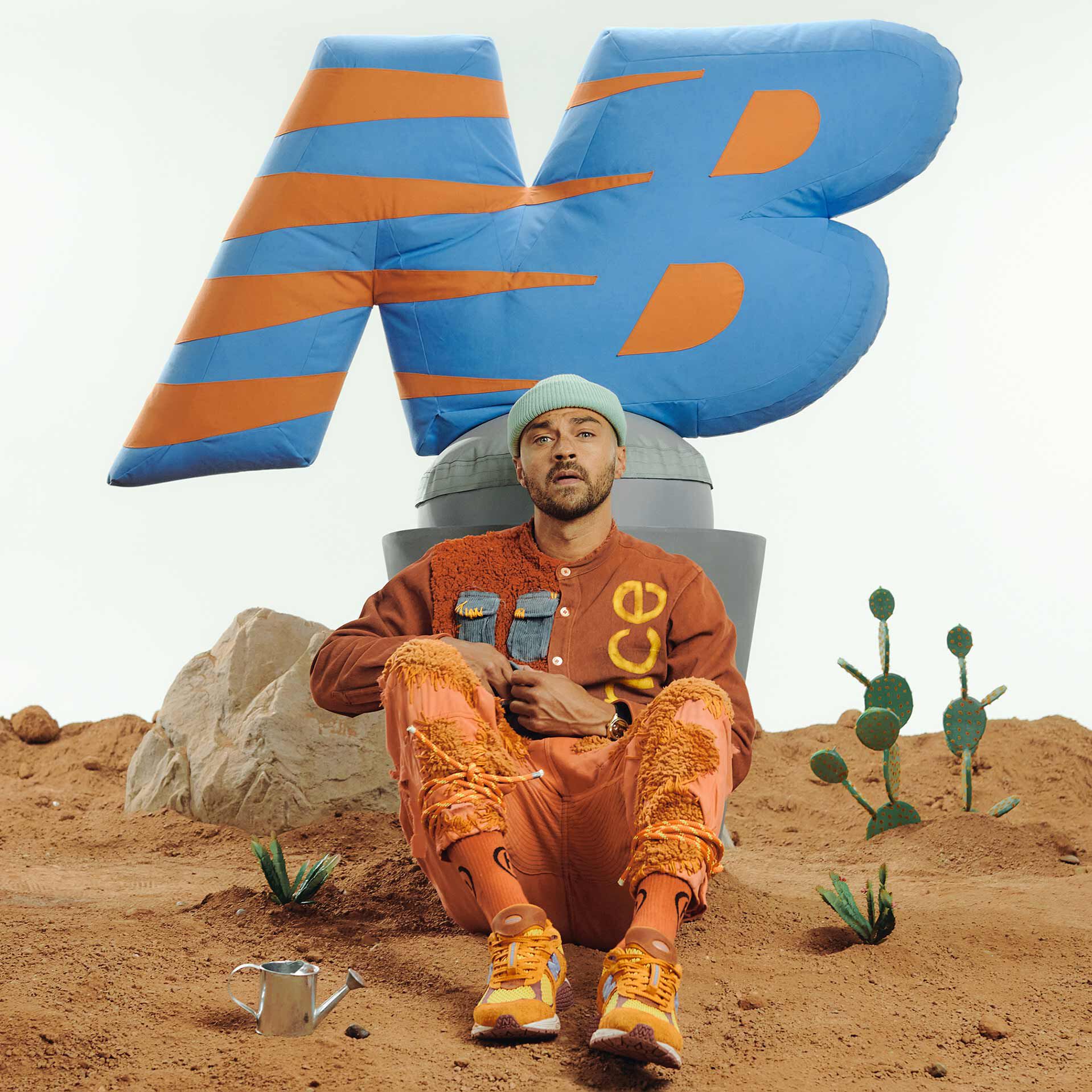 Jesse Williams sitting in a desert scene wearing an all-orange outfit and NB x Salehe Bembury 2002