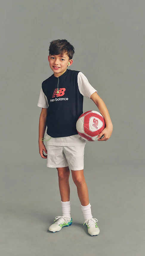 Kid holding a soccer ball against a grey studio background.