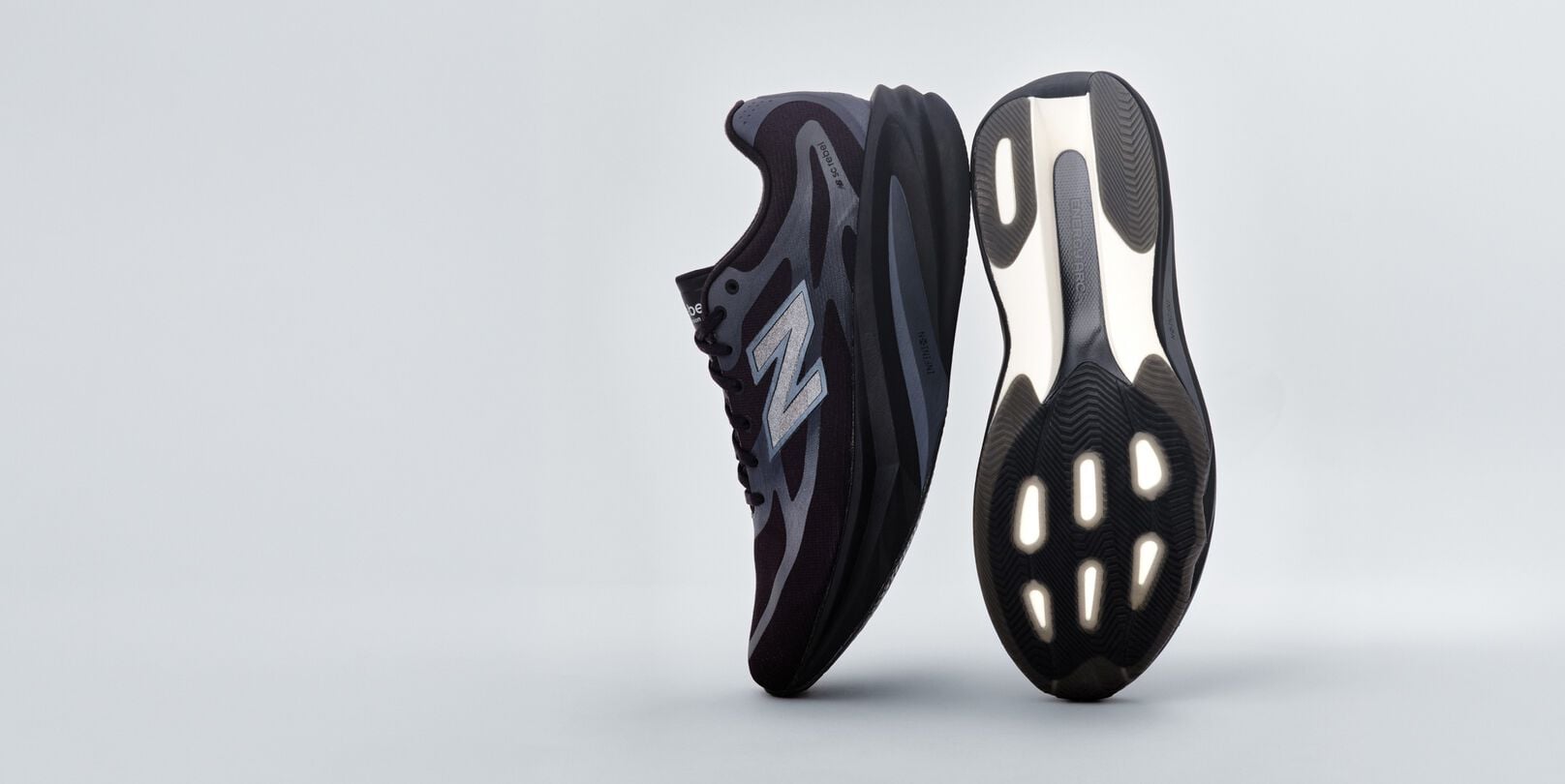 A pair of black New Balance sneakers sitting on a gray studio backdrop. 