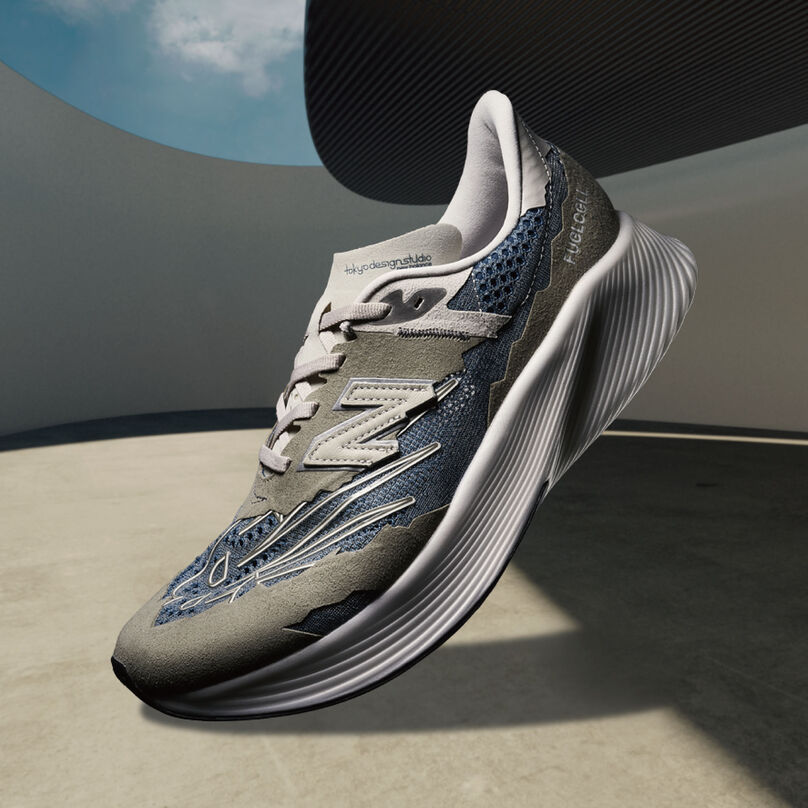 A steel grey NB x Tokyo Design Studio RC Elite running shoe floating in space in front of a 3D rendered architectural background and blue sky