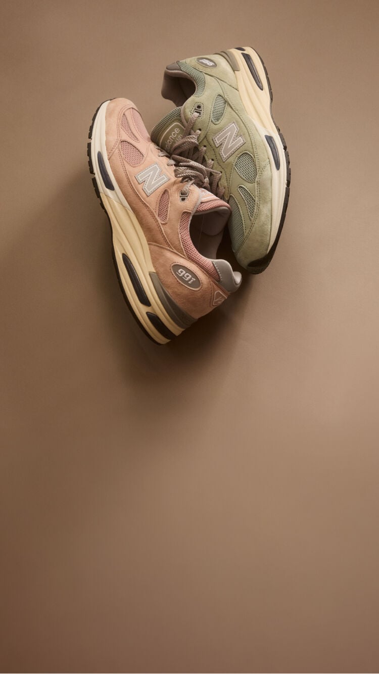 Top down view of two New Balance Made in UK sneakers resting against one another in a beige studio environment. 