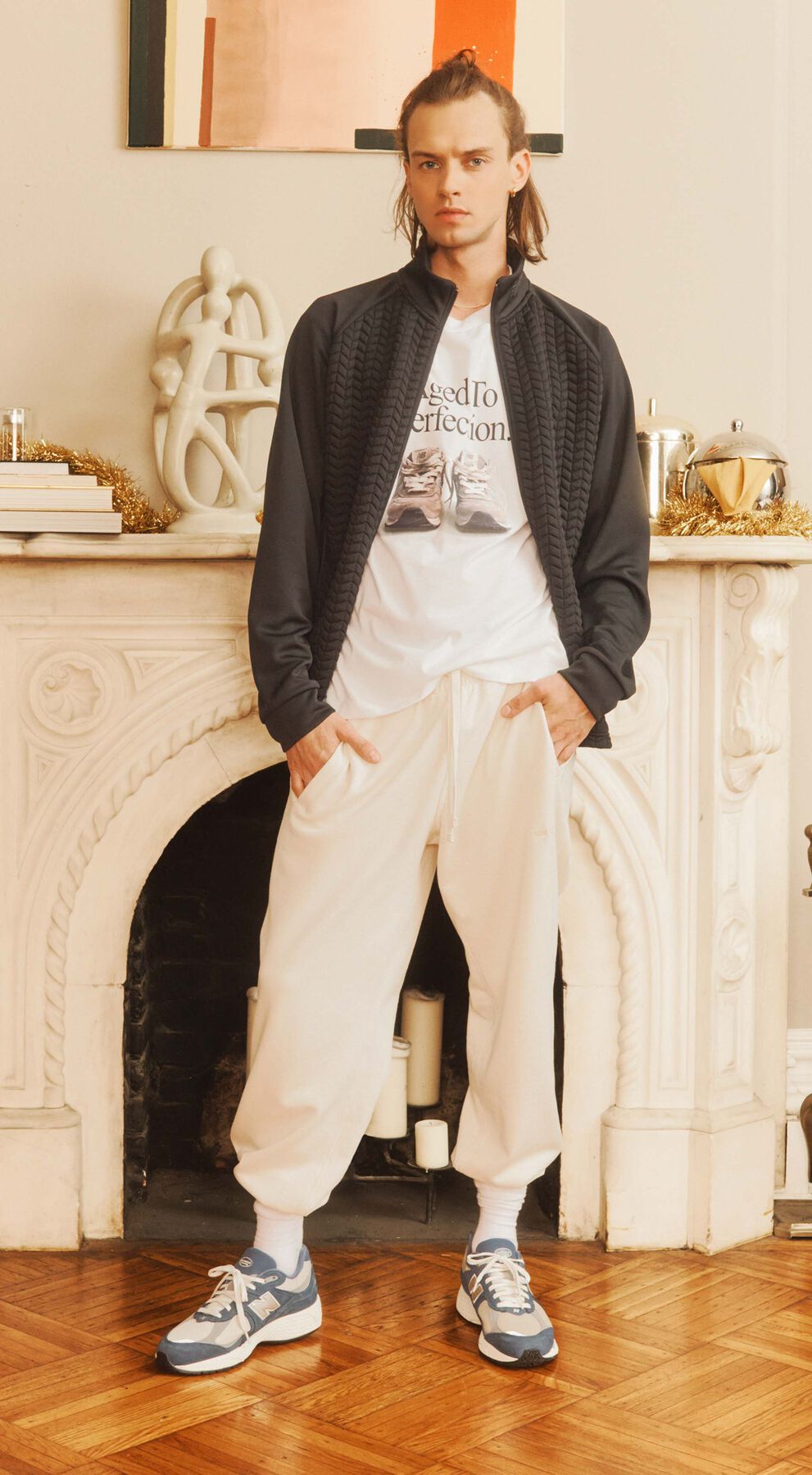 Male model wearing cold weather New Balance classic clothing and shoes posed against a decorative fireplace